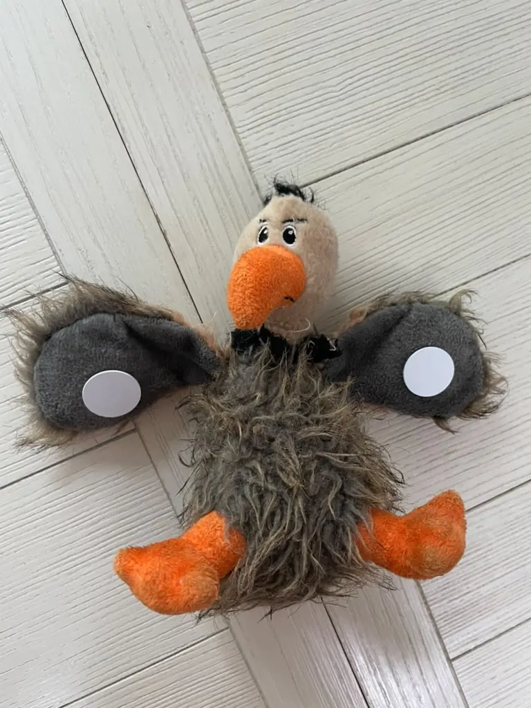 The plushie lying with its wings spread, showing a round tap tag on each wing.